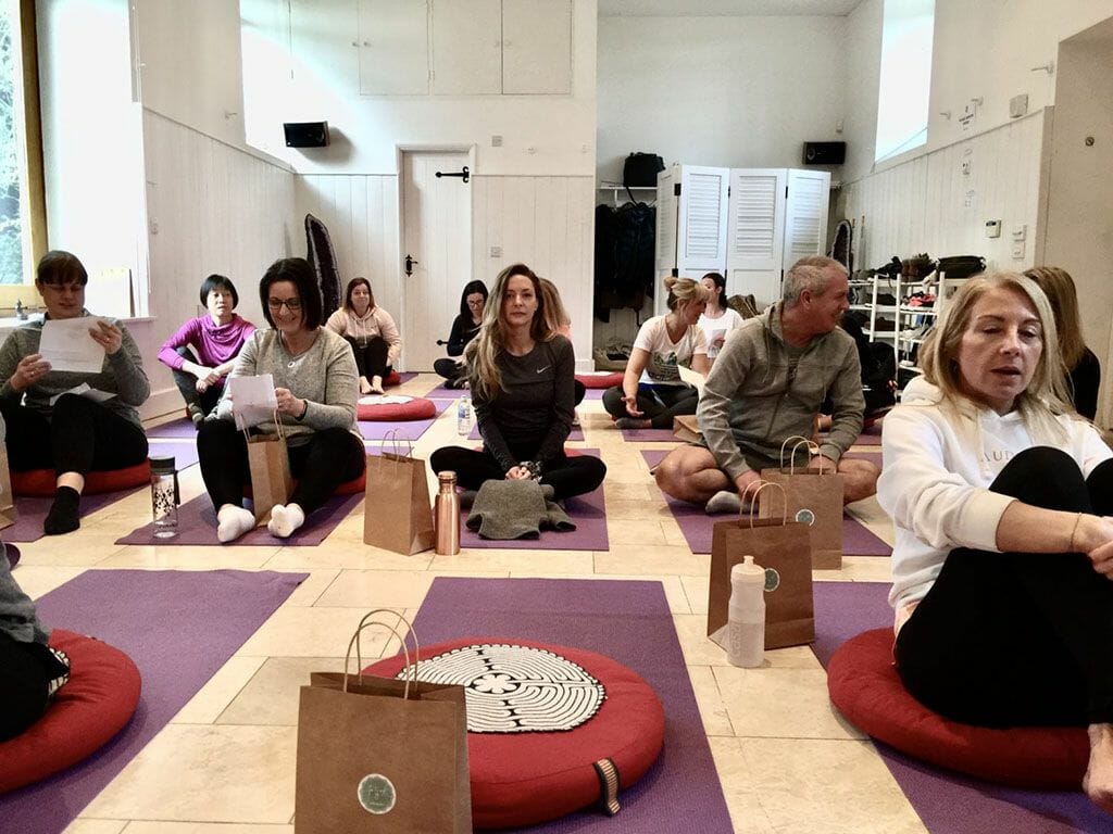 a group of people sitting in a room on yoga mats.