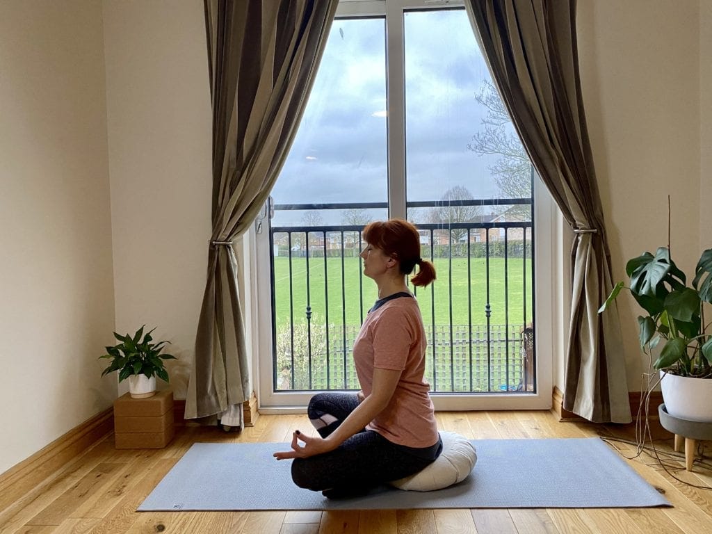 a woman sitting on a yoga mat in front of a window.