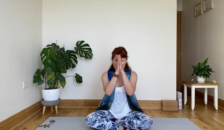 a woman sitting on a yoga mat in a room.