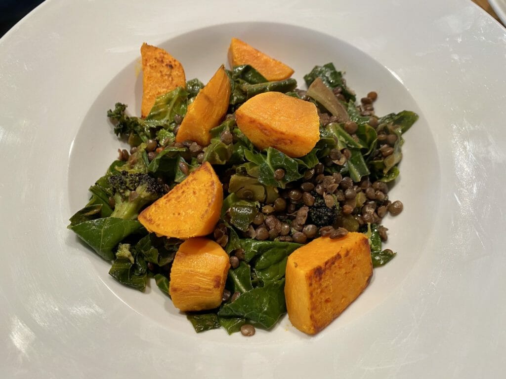 a white plate topped with a salad of greens and tofu.