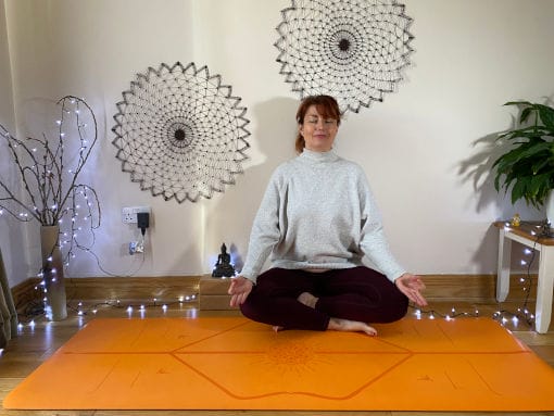 a woman sitting on a yoga mat in a room.