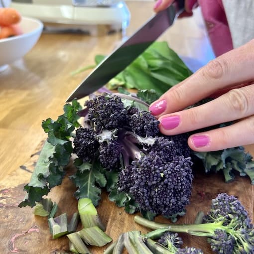 a woman is cutting up some broccoli on a cutting board. Julia is cutting up some broccoli on a cutting board.