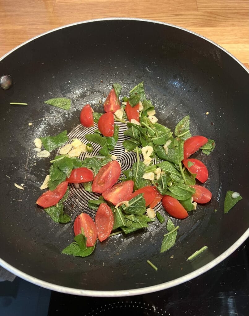 Green detox pasta with tomatoes and basil cooked in a wok on a stove.