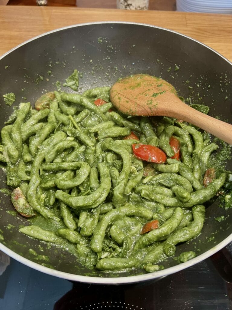 Green pesto pasta cooked in a wok and stirred with a wooden spoon.