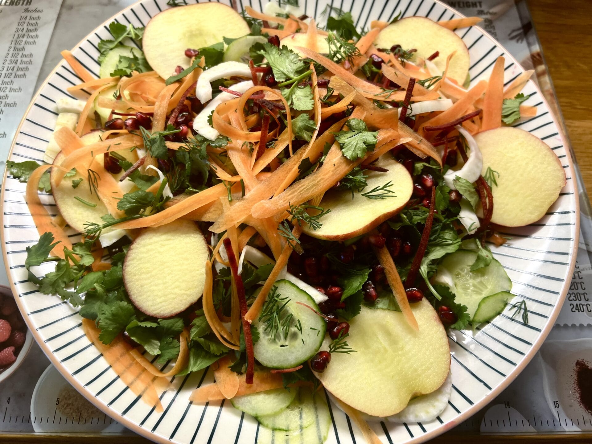 A plate of salad with carrots, cucumbers and pomegranate.