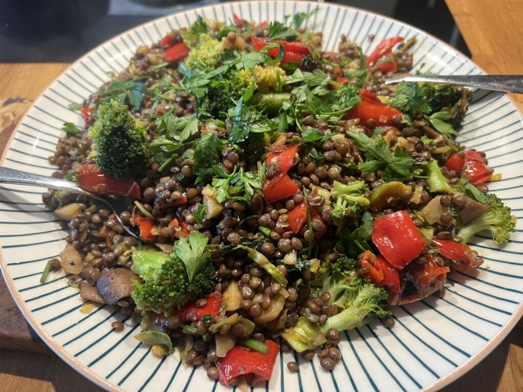 A healthy gut lunch featuring a plate of brown lentils and vegetables on a wooden table.