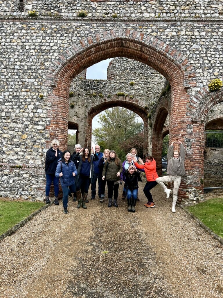 Group of people uniting in shared presence and smiling while posing together in front of ancient stone arch ruins.