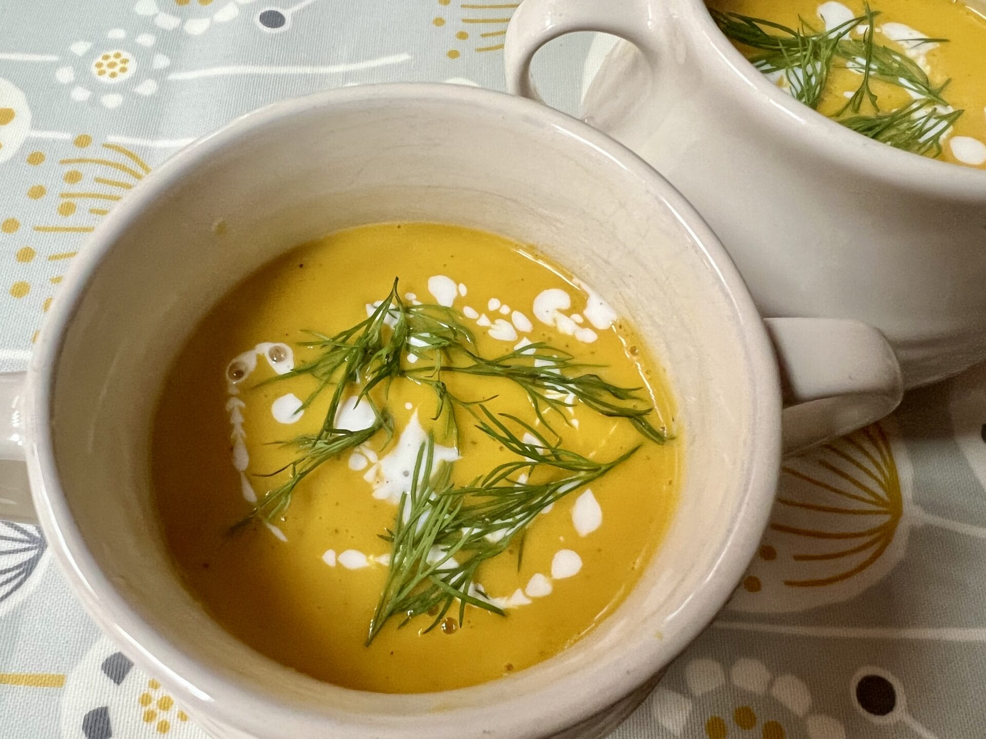 Anti-Inflammatory Carrot and Butternut Squash Soup with Turmeric, Ginger and Dill Two bowls of creamy butternut squash, carrot soup garnished with swirls of cream and fresh dill, placed on a patterned tablecloth.