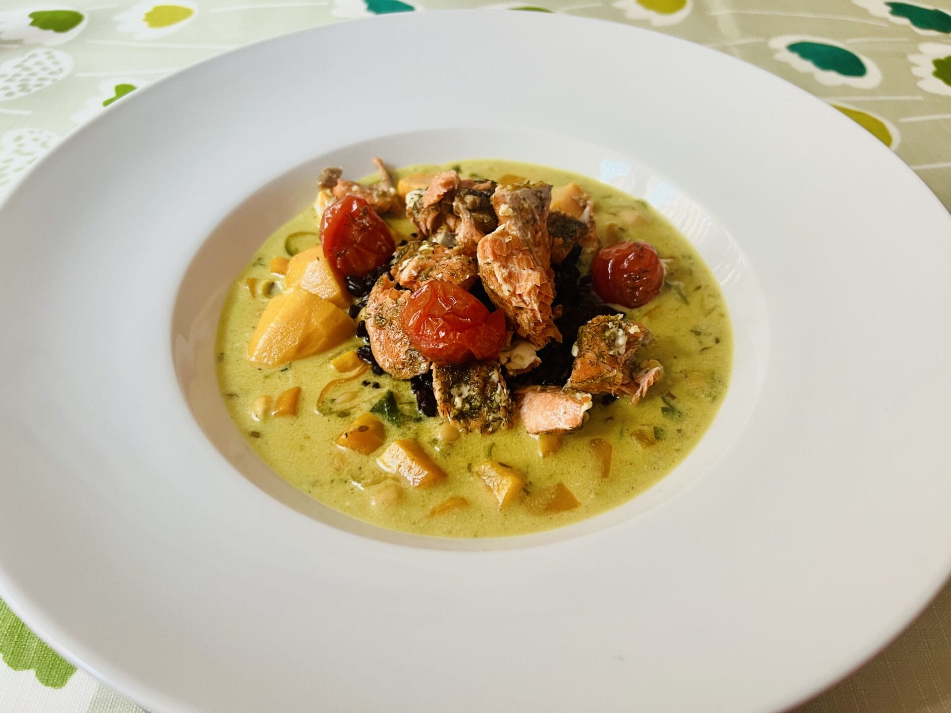 A plated dish featuring a creamy soup with chunks of fish, cherry tomatoes, and diced vegetables, presented in a white bowl.