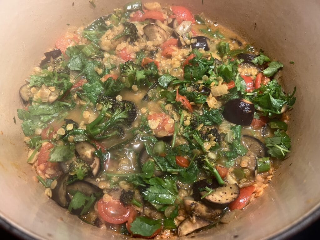 A pot of vegetable stew with cilantro, eggplant, tomatoes, and lentils.