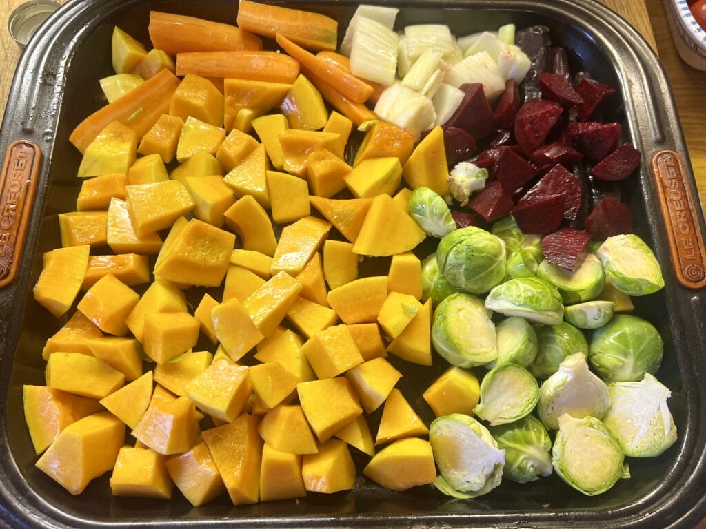 Tray of raw vegetables: cubed butternut squash, sliced carrots and fennel, diced beets, and halved Brussels sprouts.