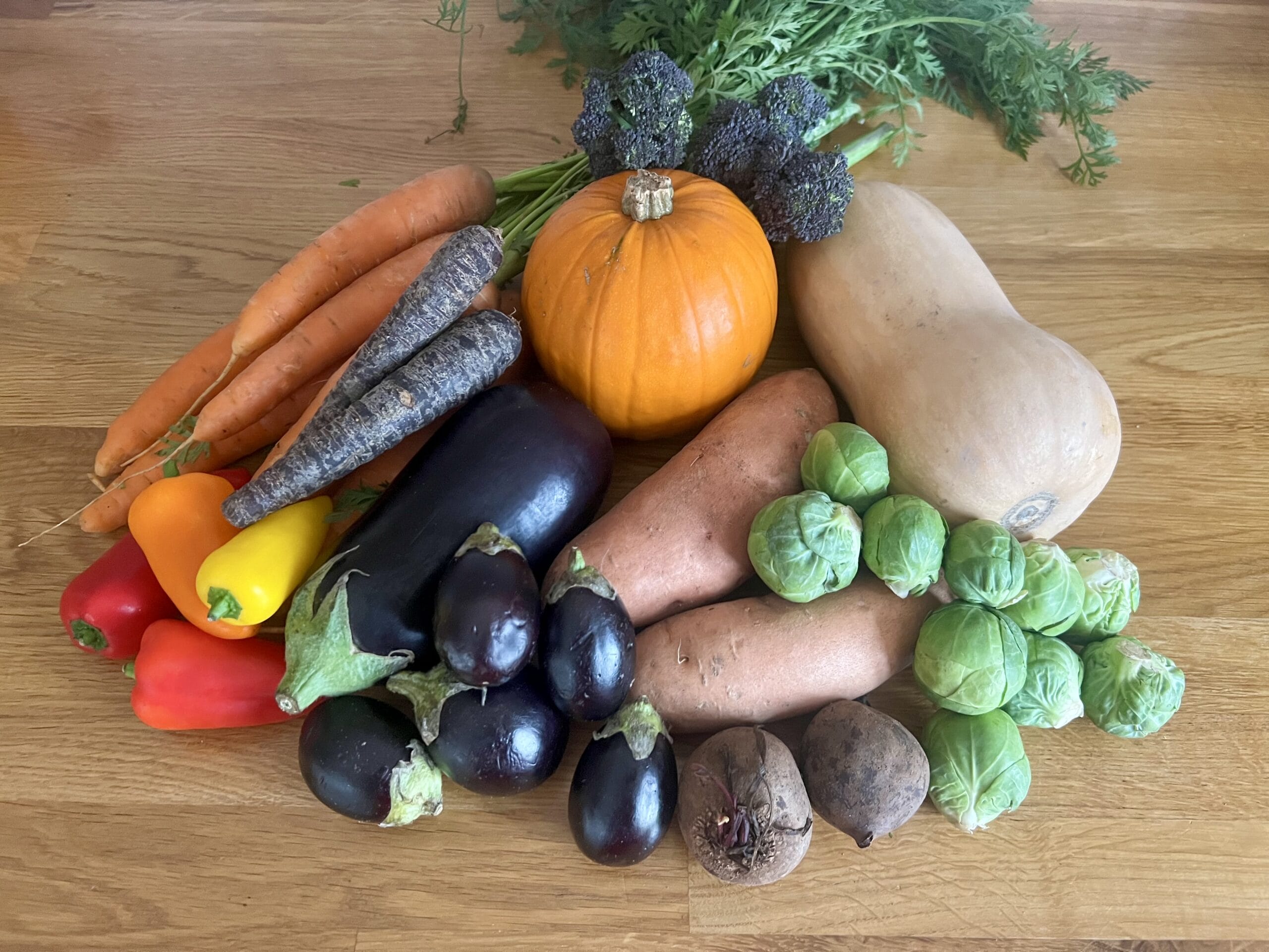 A vibrant array of seasonal superfoods including carrots, bell peppers, eggplants, a pumpkin, broccoli, butternut squash, sweet potatoes, Brussels sprouts, and beets are artfully arranged on a wooden surface to nourish your soul with autumn's harvest.