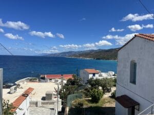 Coastal view with white buildings, blue sea, and mountainous shoreline under a clear sky.