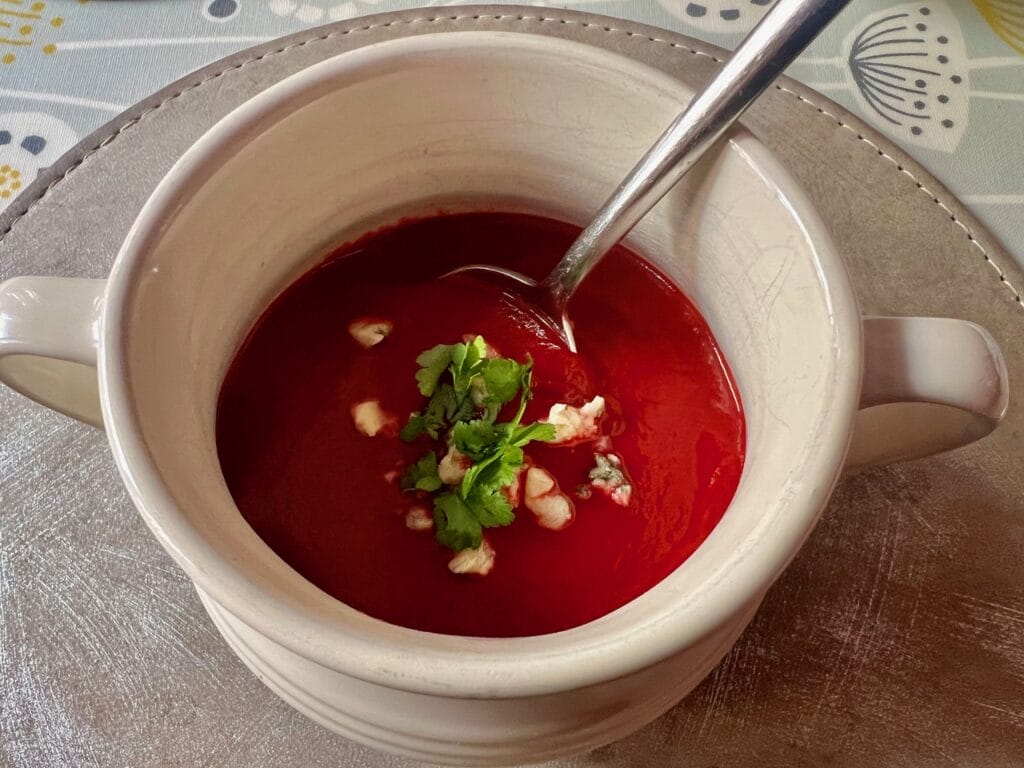 A bowl of tomato soup garnished with cilantro and chopped nuts, with a spoon resting inside.
