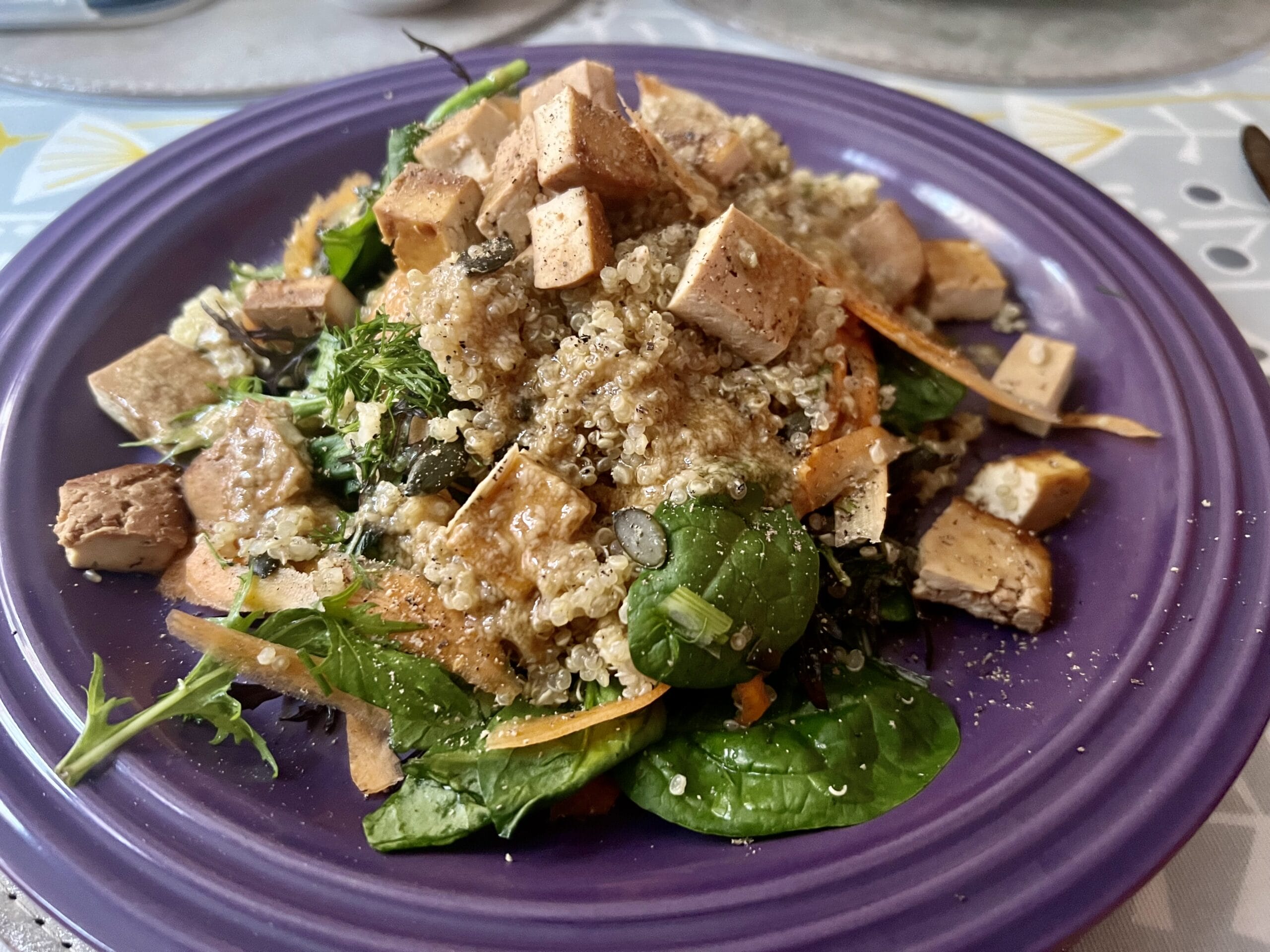 A purple plate with quinoa salad, tofu cubes, spinach, and leafy greens to fuel your day and lighten your nights for better energy. A purple plate with quinoa salad, tofu cubes, spinach, and leafy greens to fuel your day and lighten your nights for better energy.