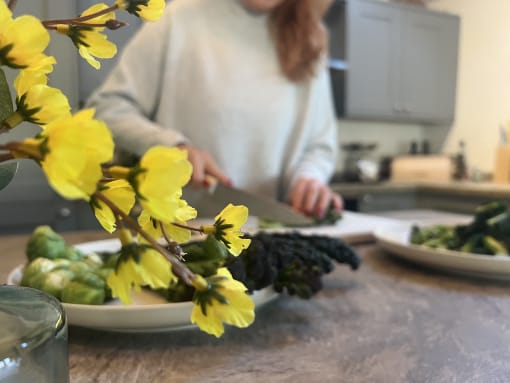 Person chopping vegetables in a kitchen, with yellow flowers in the foreground.