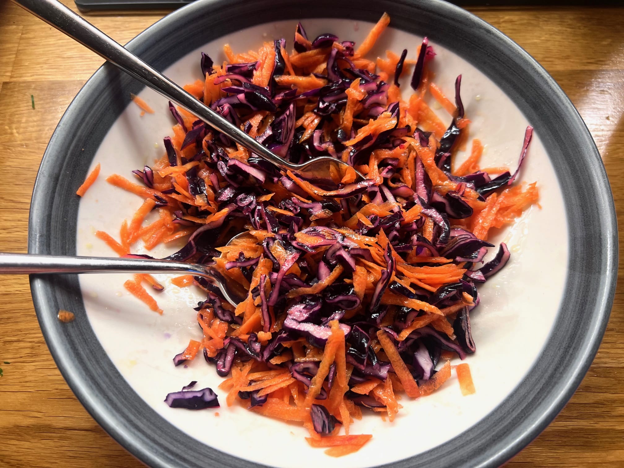 Bowl of shredded red cabbage and carrots with two metal forks on a wooden table. Bowl of shredded red cabbage and carrots with two metal forks on a wooden table.