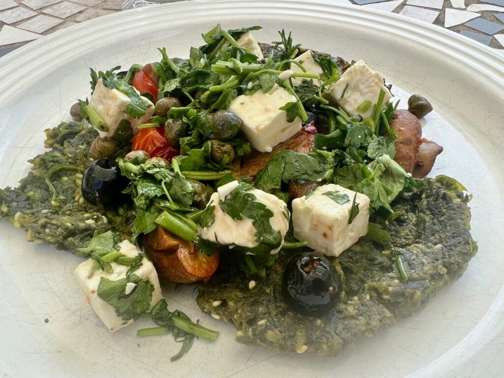 Green Detox Delight: Wild garlic pancakes are topped with fresh greens, cubes of feta cheese, tomatoes, olives, capers, and herbs for a vibrant Mediterranean garnish.