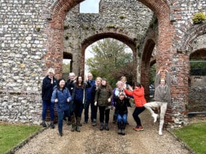 A group of people pose and smile in front of the arched stone ruins of an old building, with greenery visible in the background.