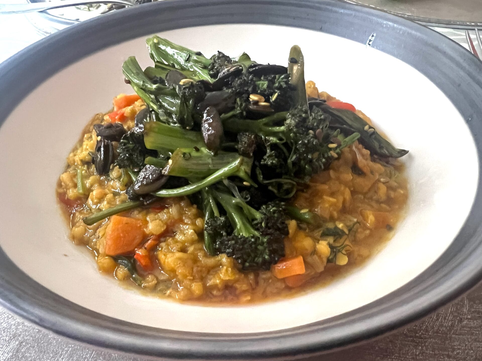 A bowl of vegetable stew with chopped carrots, lentils, and leafy greens, topped with sautéed broccolini and mushrooms.