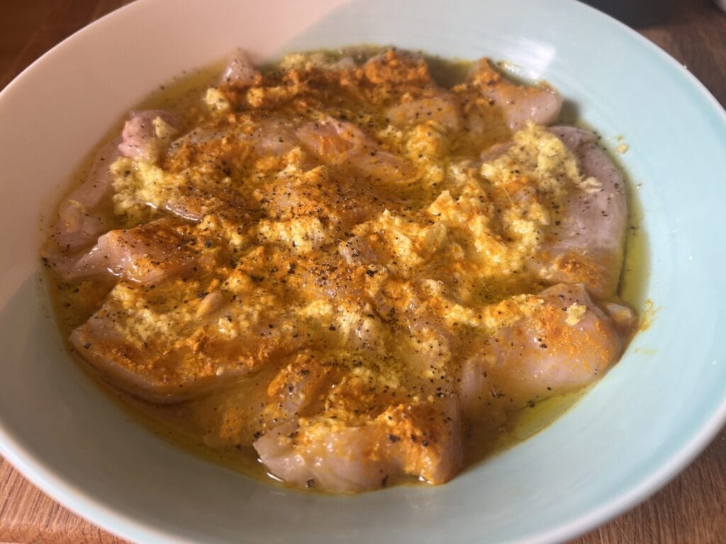 Raw chicken pieces marinating in a bowl with yellow spices, minced garlic or ginger, black pepper, and oil create a glutamine-rich gut healing dish perfect for supporting digestion and overall wellness.