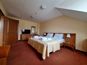 A hotel room with a double bed, two bedside tables with lamps, a TV on a cabinet, an open door, and a folded bathrobe on the bed.