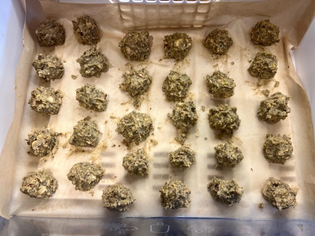 Thirty raw, irregularly-shaped Pistachio–Cashew Superfood Chocolate Bites are arranged in rows on a parchment-lined baking sheet, ready for baking.